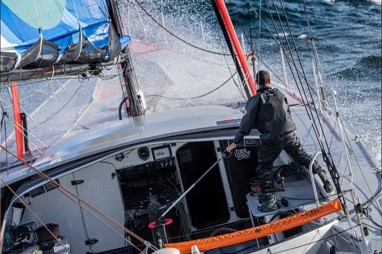 Skipper barrant son Imoca debout sur le pont, de dos